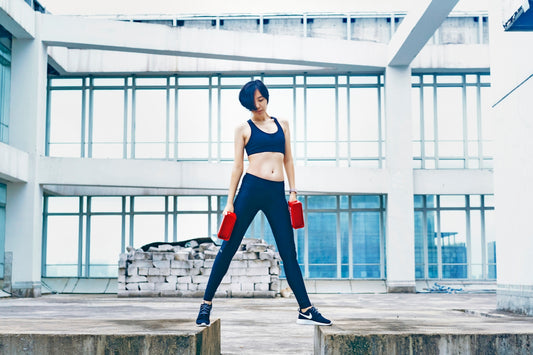 woman wearing black sports bra and pants while holding two red weights