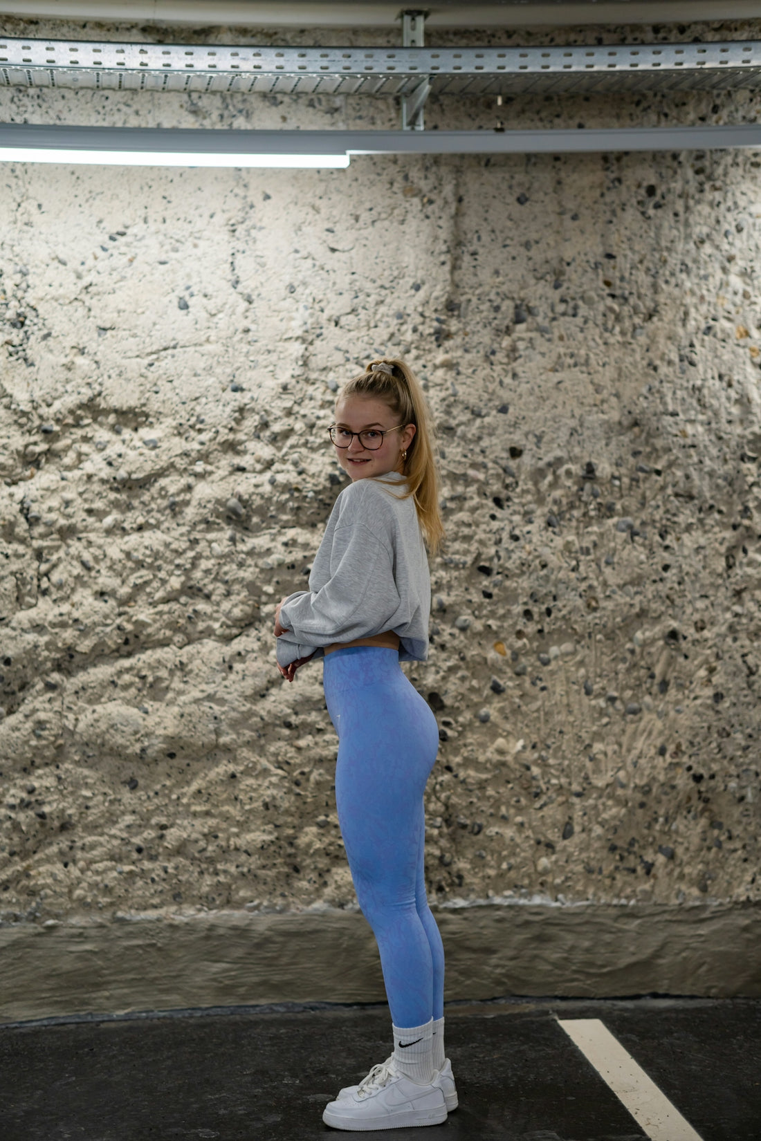 a woman standing in a parking lot wearing blue leggings