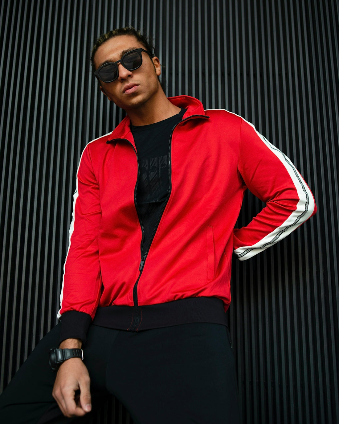a man in a red jacket and sunglasses leaning against a wall