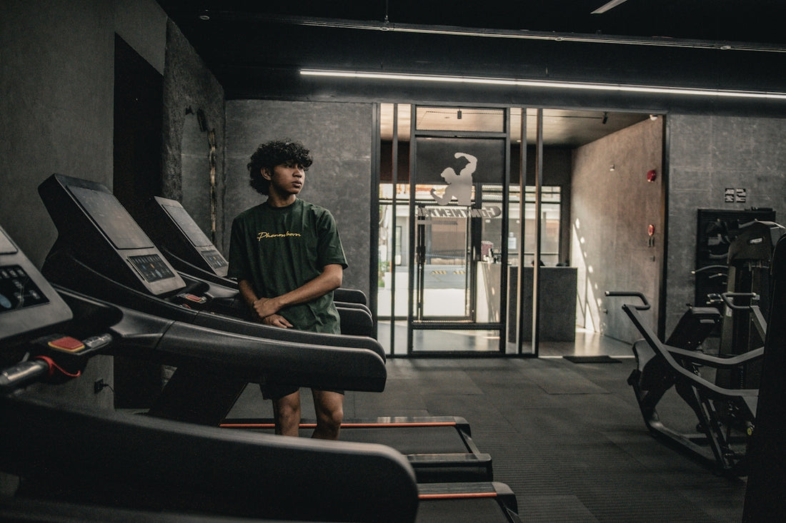 A man standing in a gym next to a row of treadmills