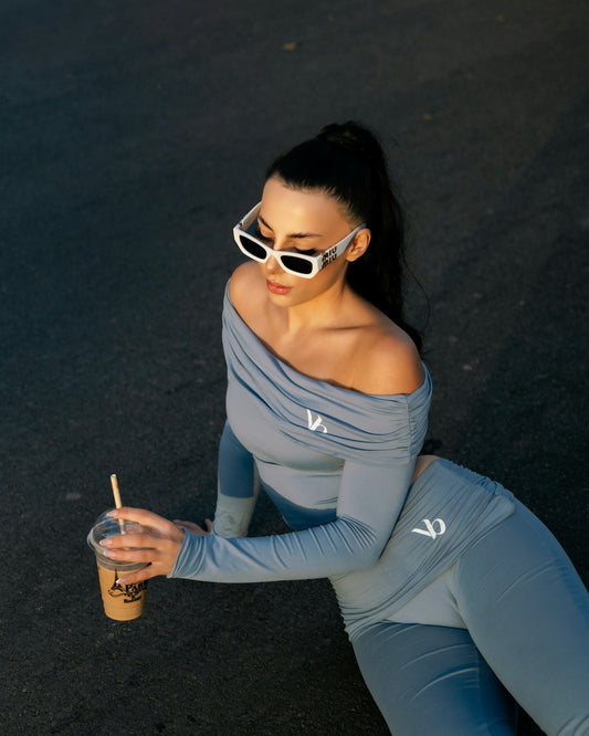 Woman in blue outfit with sunglasses holds coffee