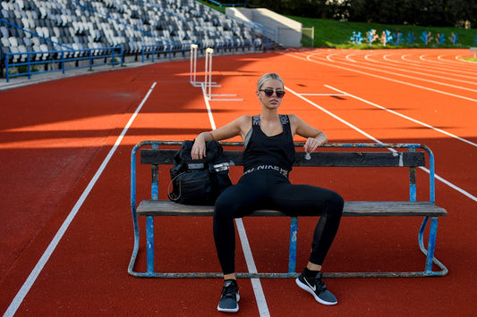 Woman in sportswear resting on bench at stadium track.