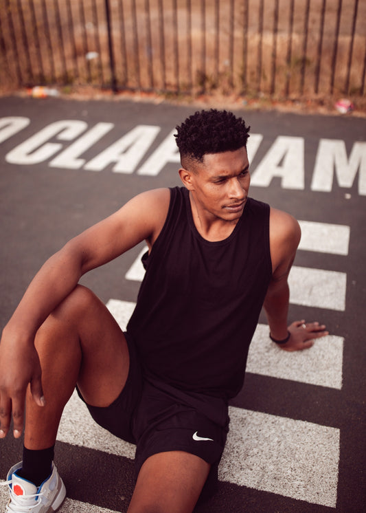 Young man in black athletic wear sits on striped pavement.