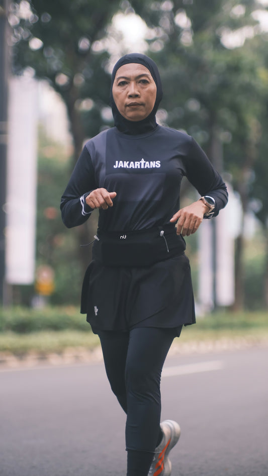 A woman in a black hijab and athletic wear running on a city street