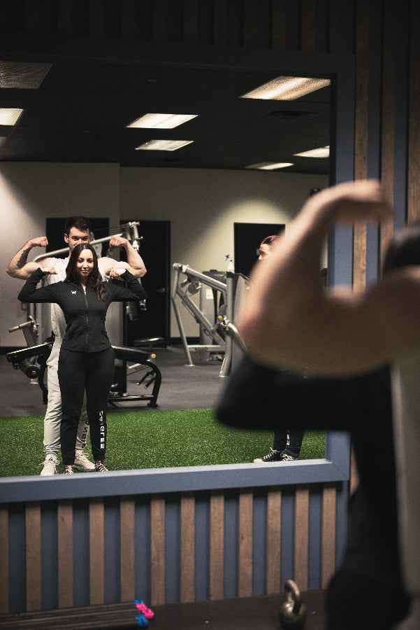 Two people exercising in a gym with a mirror reflecting their actions.