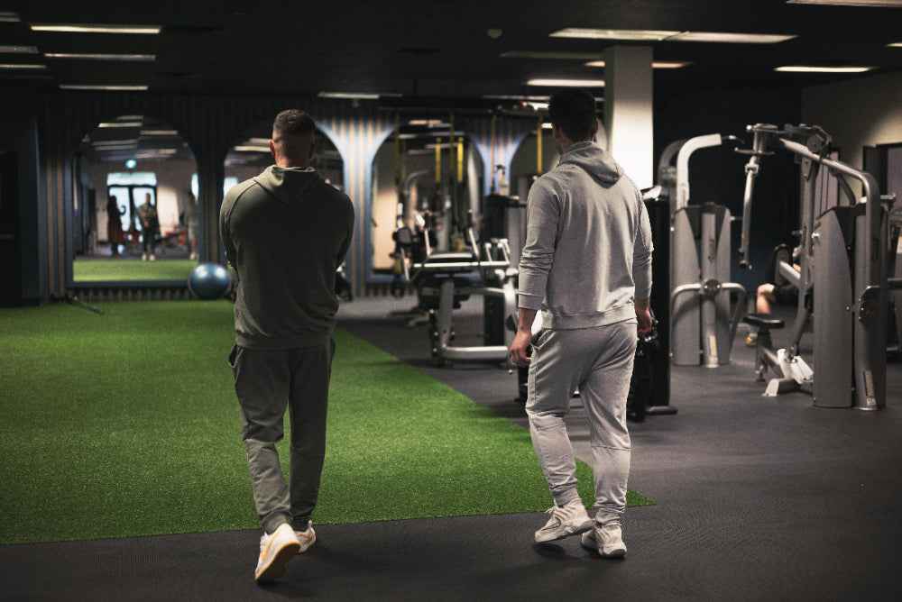 Two people walking through a modern gym with exercise equipment.