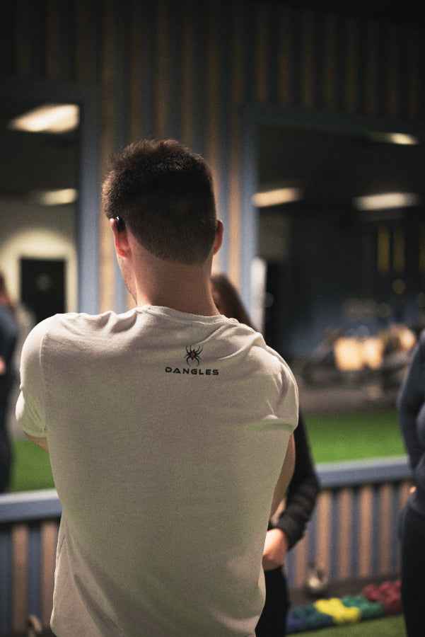 Person wearing a white t-shirt with a logo, standing in an outdoor setting.