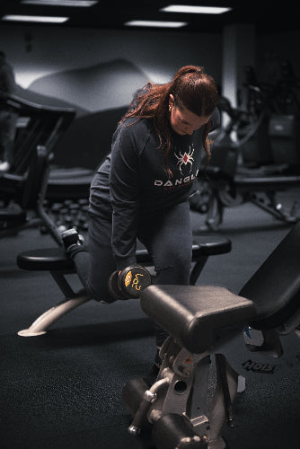 Person lifting weights in a gym setting with 'Dang' branded shirt