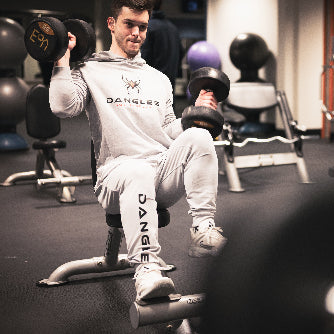 Person exercising with dumbbells in a gym wearing a 'Dangles' branded outfit.