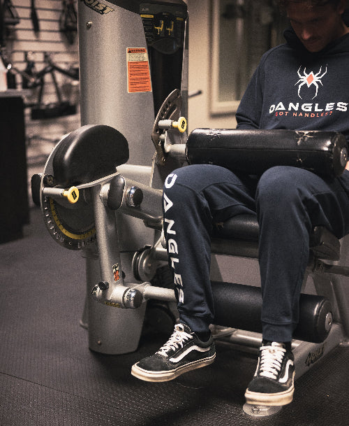 Person using a leg press machine in a gym wearing a 'Dangles Got Handles' shirt.