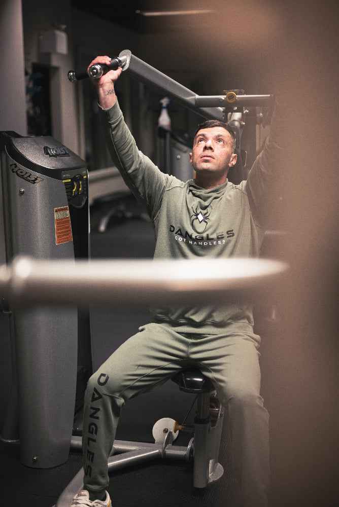 Person exercising on a machine in a gym wearing a green outfit with 'Danglies' branding.