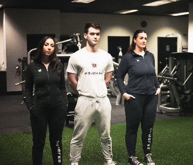 Three people standing in a gym wearing branded clothing